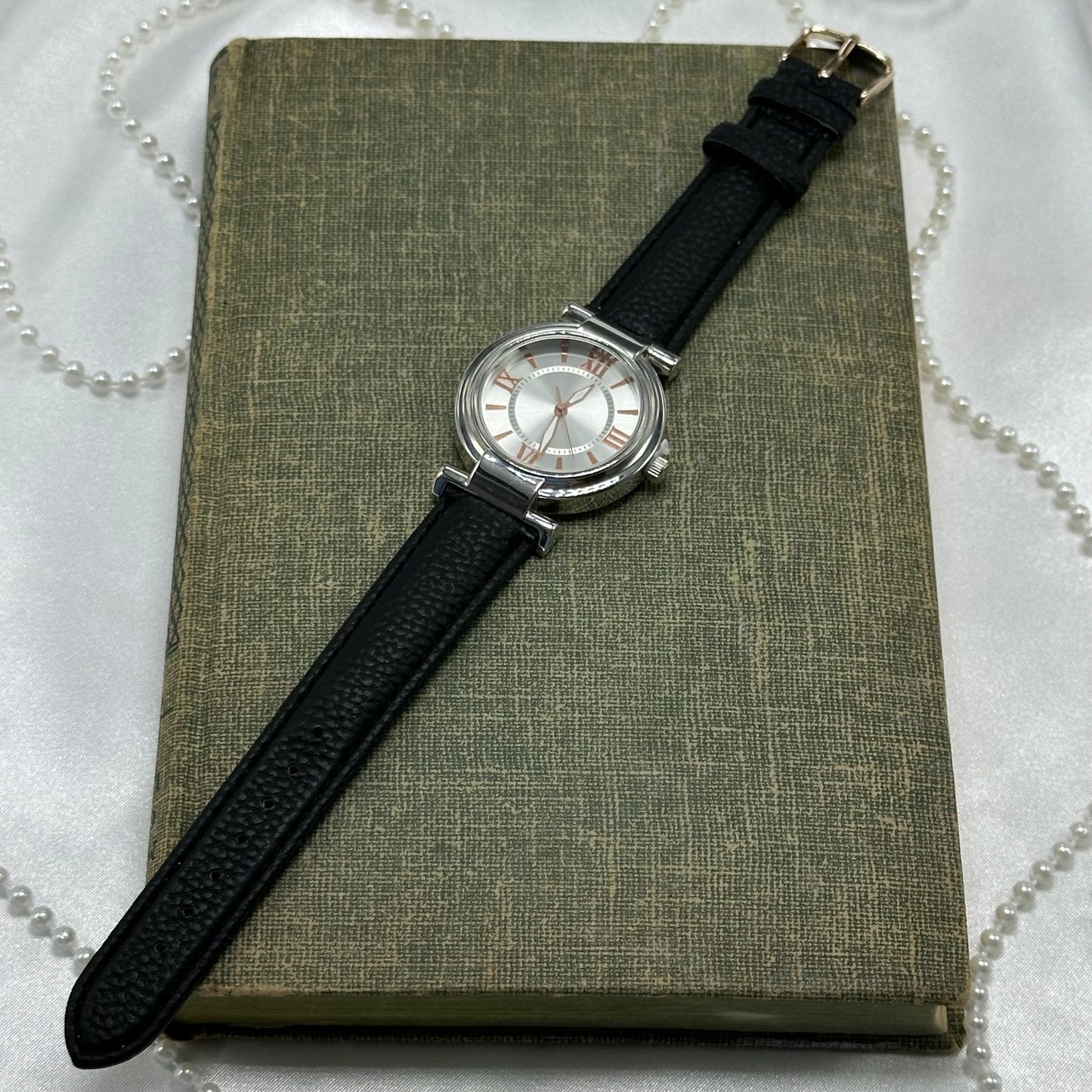 Classic round dial silver tone watch with rose gold dial details and black leather band. Watch has never been worn.
