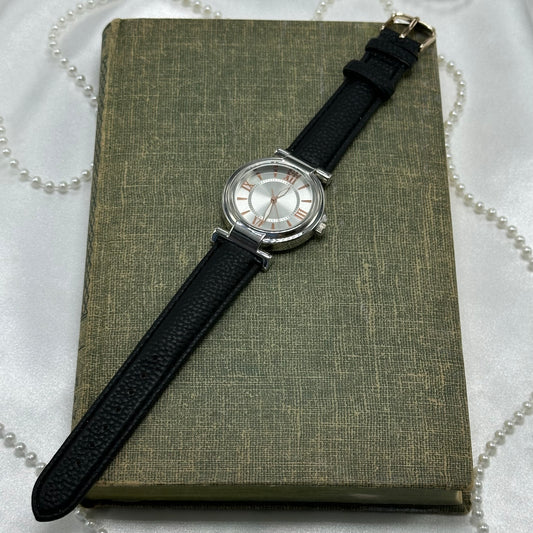 Classic round dial silver tone watch with rose gold dial details and black leather band. Watch has never been worn.