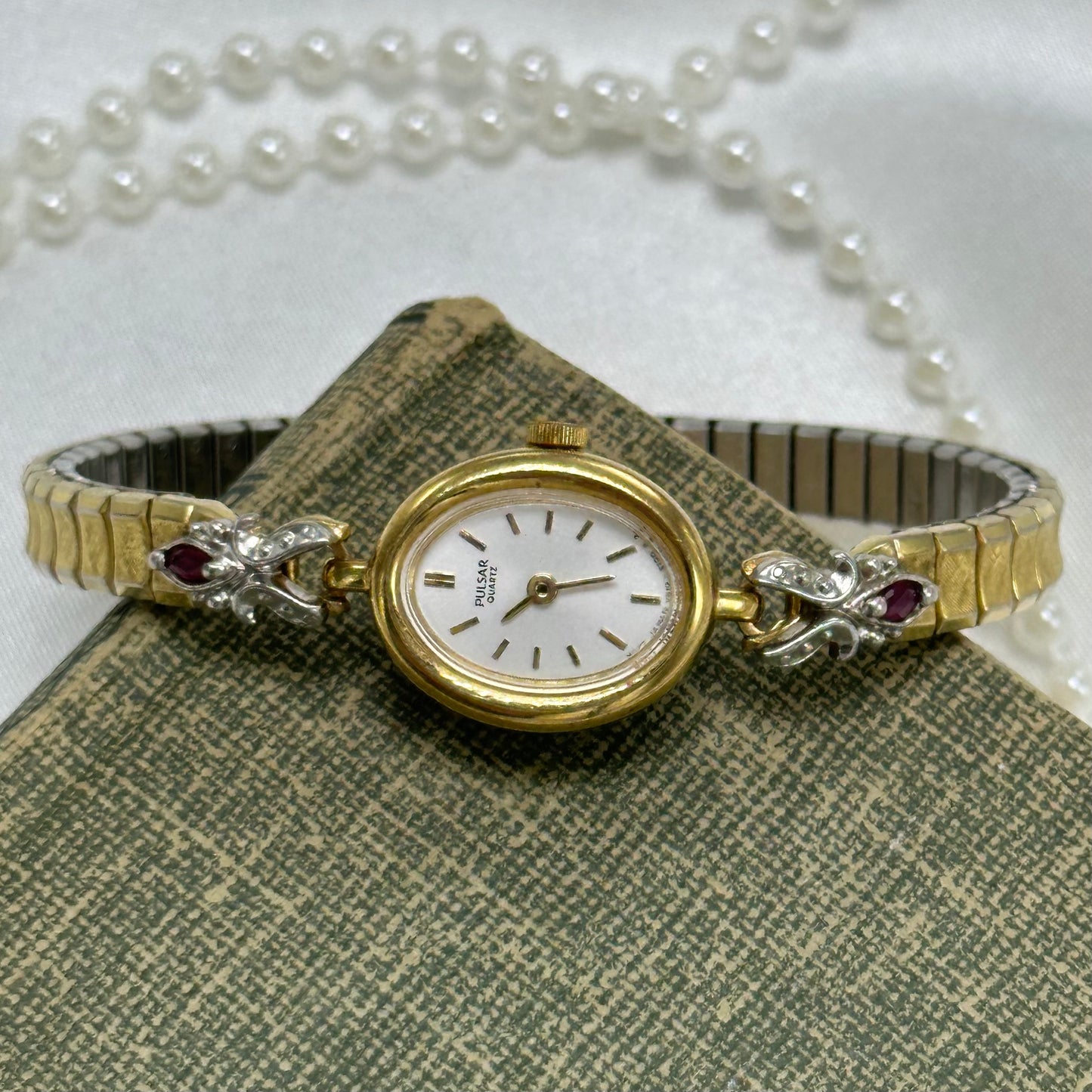 Dainty vintage gold tone oval dial Pulsar watch with quartz movement and synthetic ruby band.