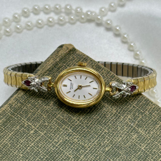 Dainty vintage gold tone oval dial Pulsar watch with quartz movement and synthetic ruby band.