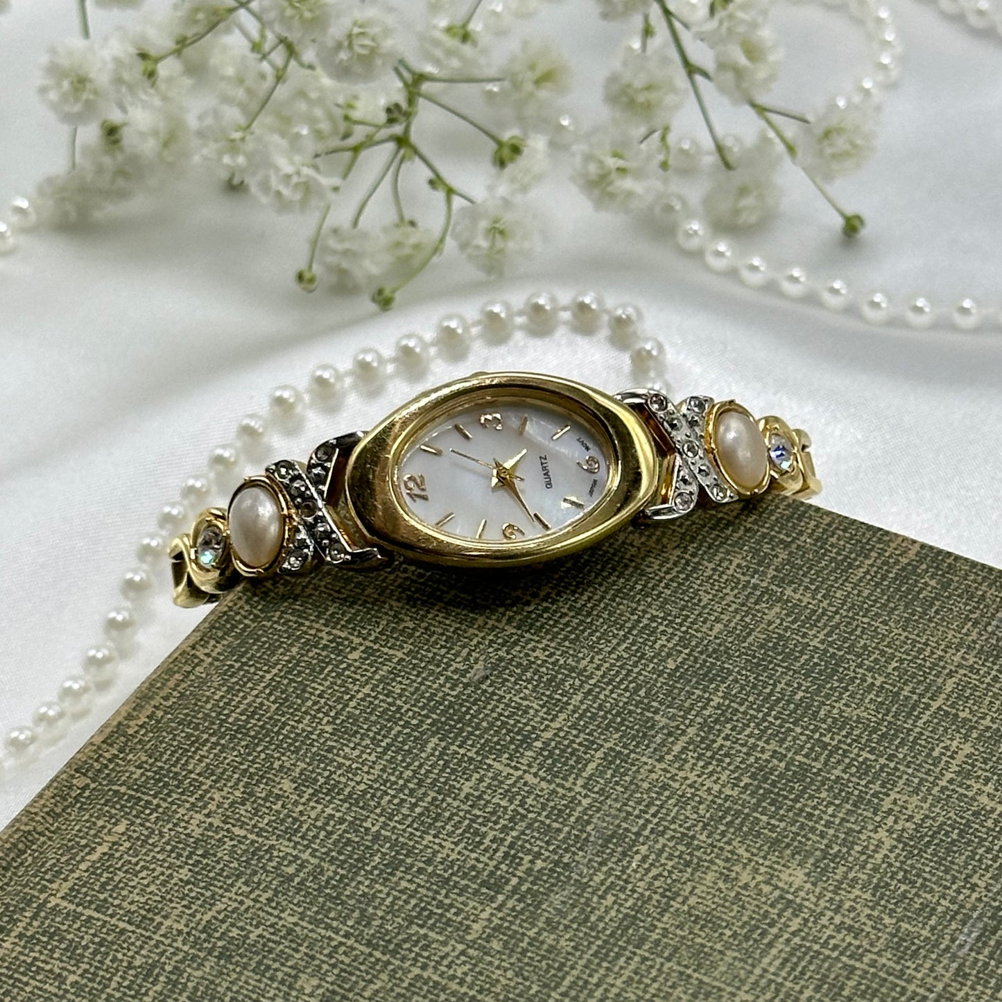 Gold tone diamanté and pearl Avon watch with quartz movement and stretchable band.