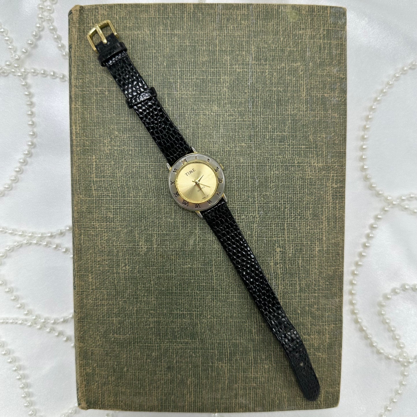 Gold tone round dial Time watch with roman numeral markers and black leather band.