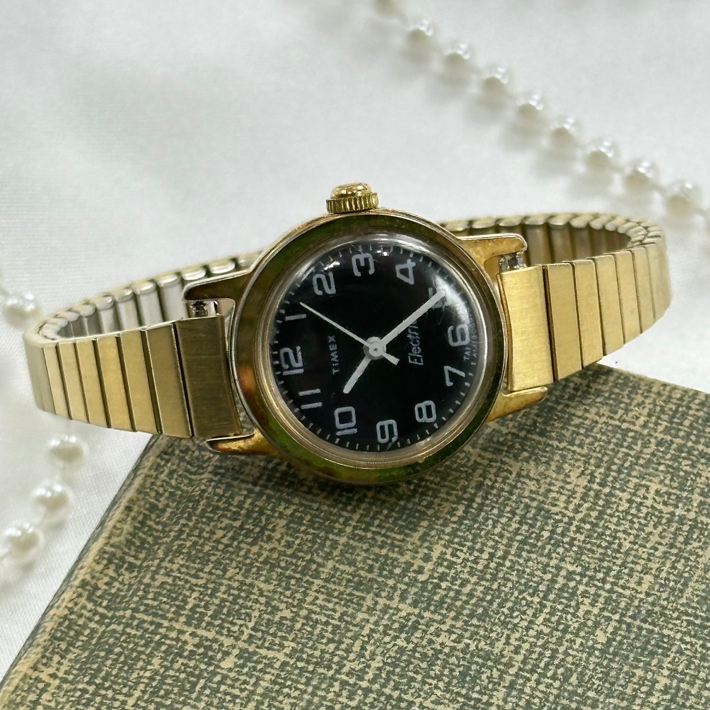 Gold tone vintage Timex electric watch with black dial and stretchable band.