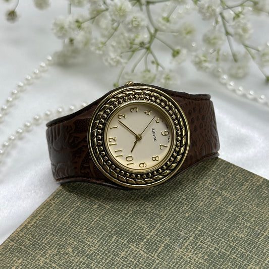 Vintage gold tone Avon cuff watch with brown leather band and quartz movement.