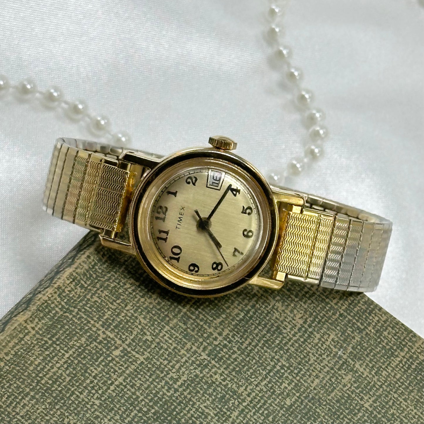 Vintage gold tone Timex manual winding watch with date display and stretchable band.