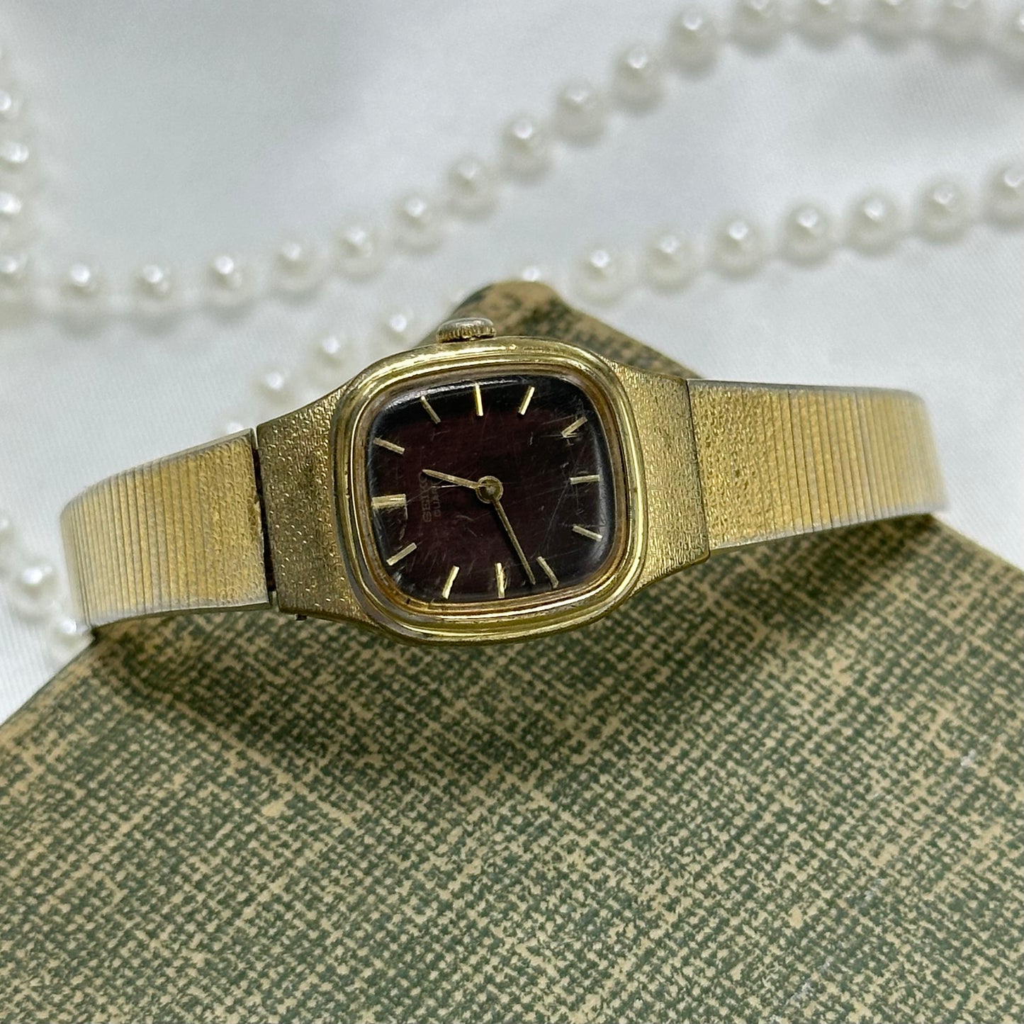 Vintage gold tone dainty Seiko watch with unique brown square dial and clasp band.