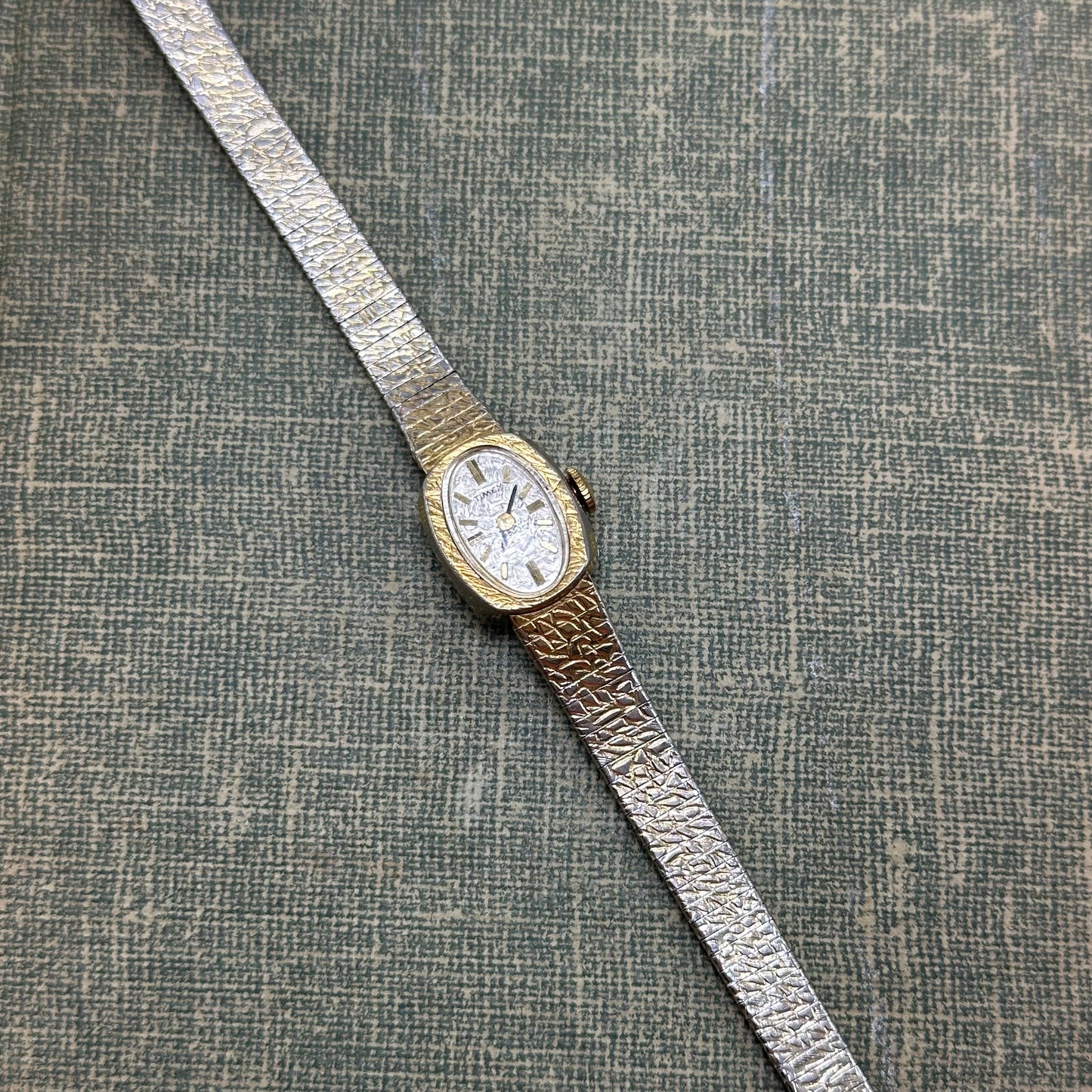 Vintage gold tone mechanical winding Timex watch with oval dial and clasp band.