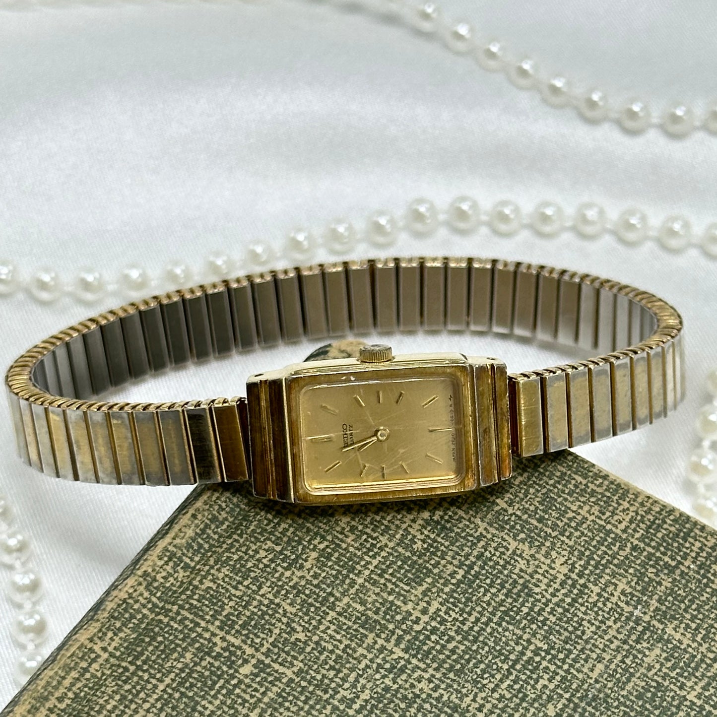 Vintage gold tone rectangle dial Seiko watch with quartz movement and stretchable band.