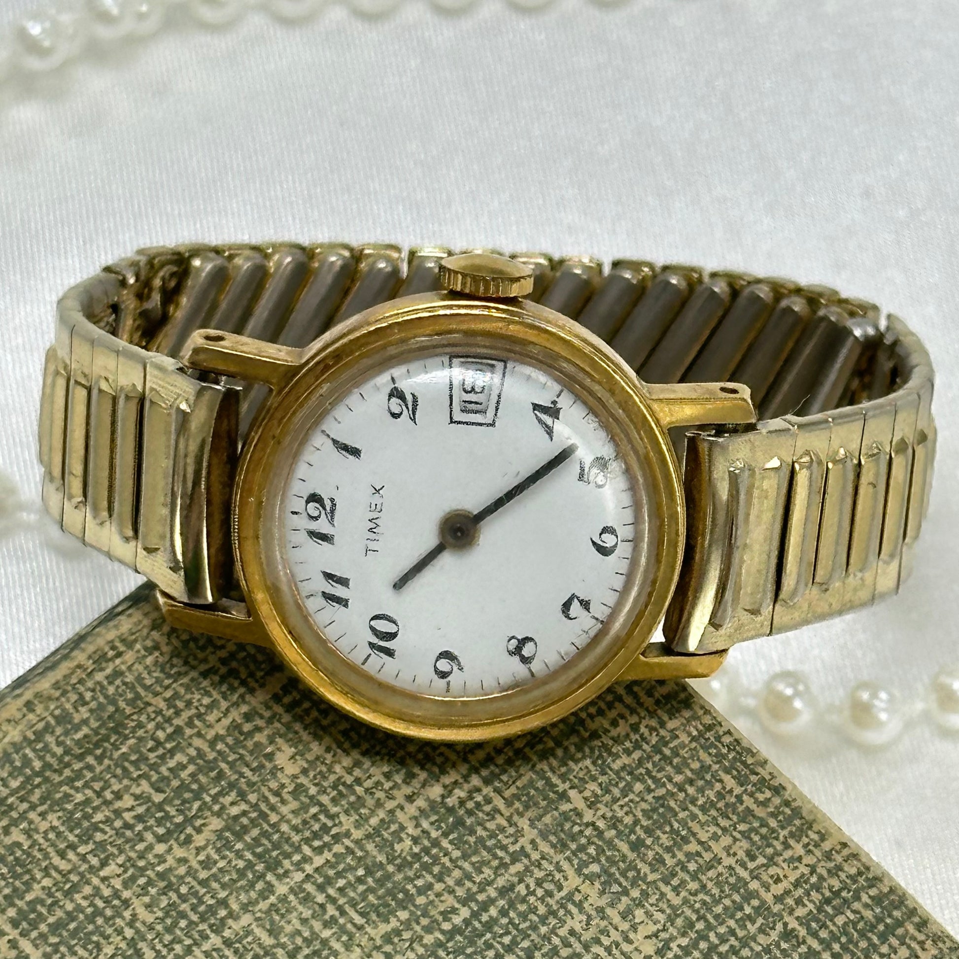 Vintage gold tone round dial manual winding Timex watch with unique stretchable band and date display.