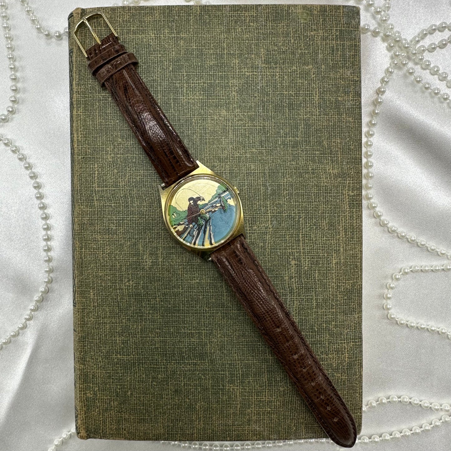 Vintage gold tone watch with unique picture of man fly fishing and quartz movement. Fish does not move