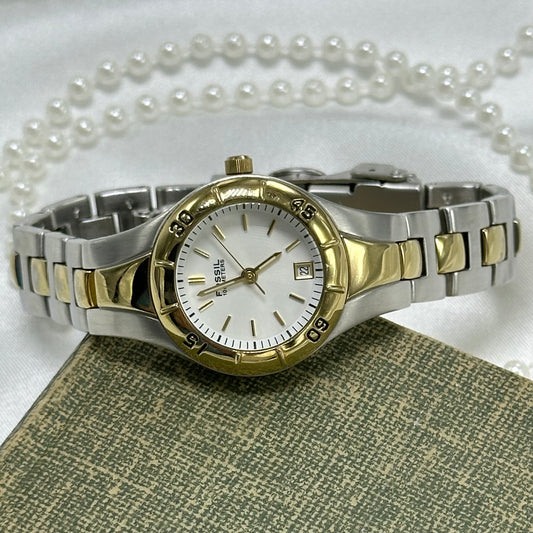Vintage silver and gold tone round dial Fossil watch with double locking fold over clasp and date display. Hands are luminous. Numbers around the dial spin. Water resistant up to 330 ft (100 meters).