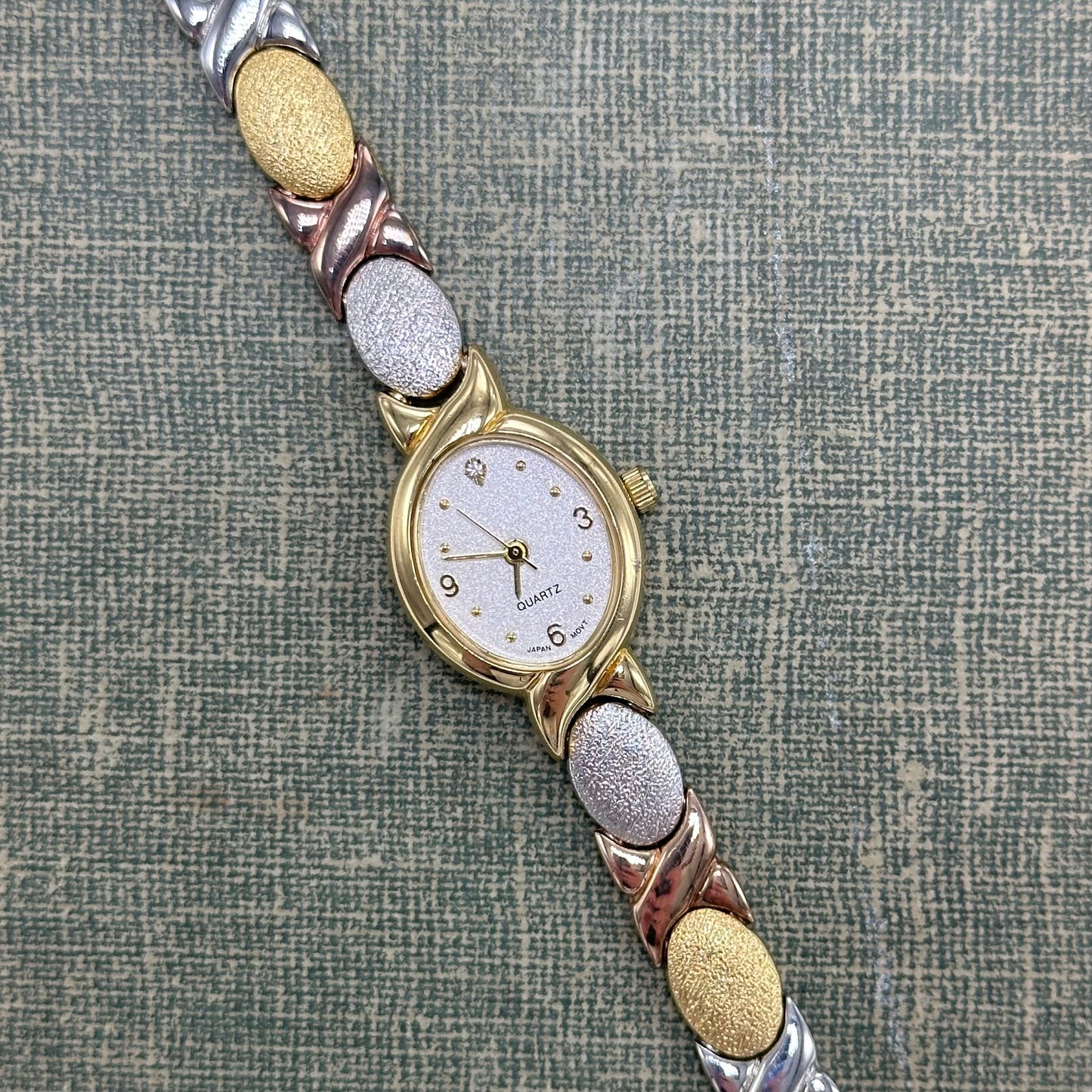 Vintage silver, gold, and bronze tone Avon watch with XO clasp band and oval dial.