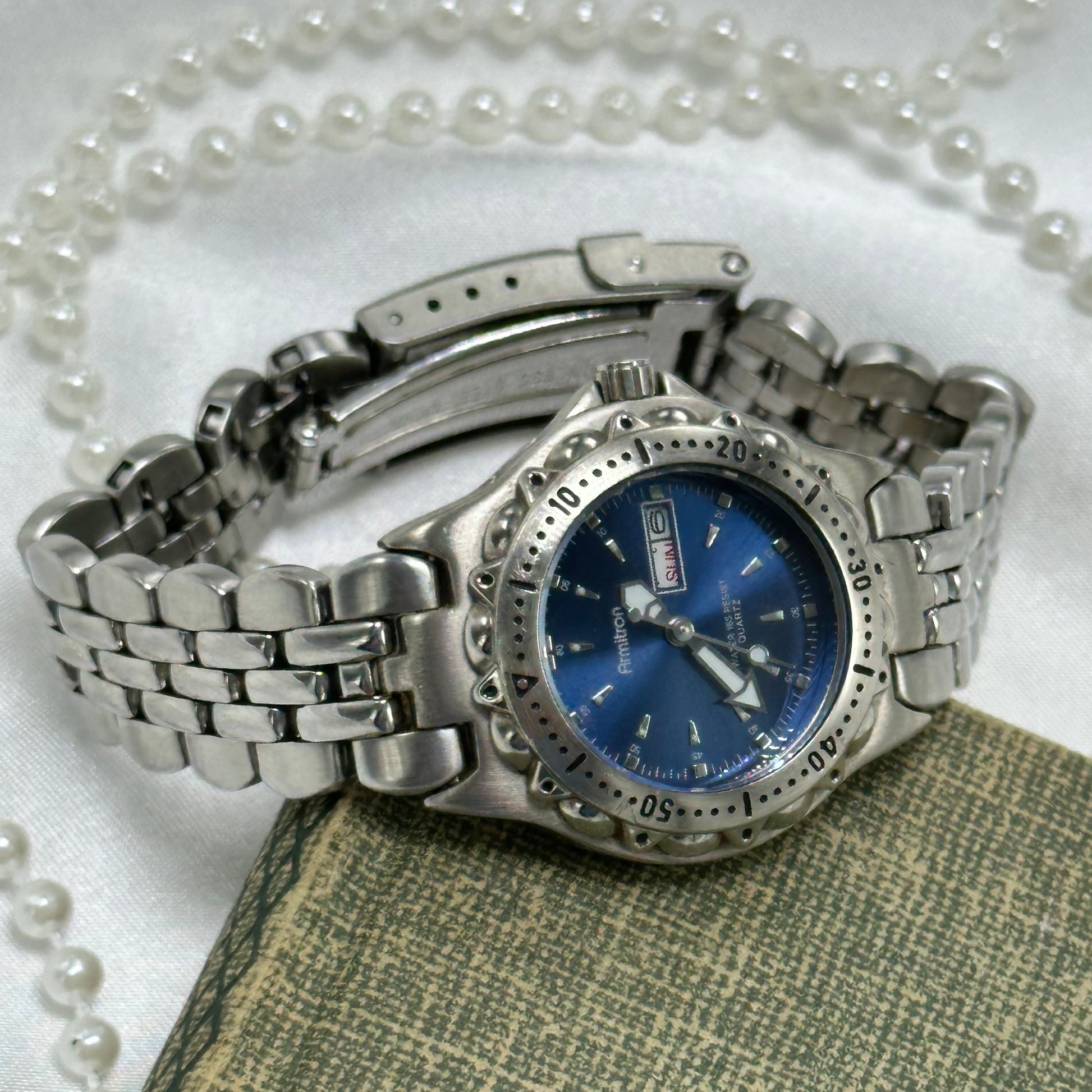 Vintage silver tone blue dial Armitron watch with double locking fold over clasp and date display. Hands are luminous. Numbers around the dial spin. Water resistant up to 330 ft (100 meters).