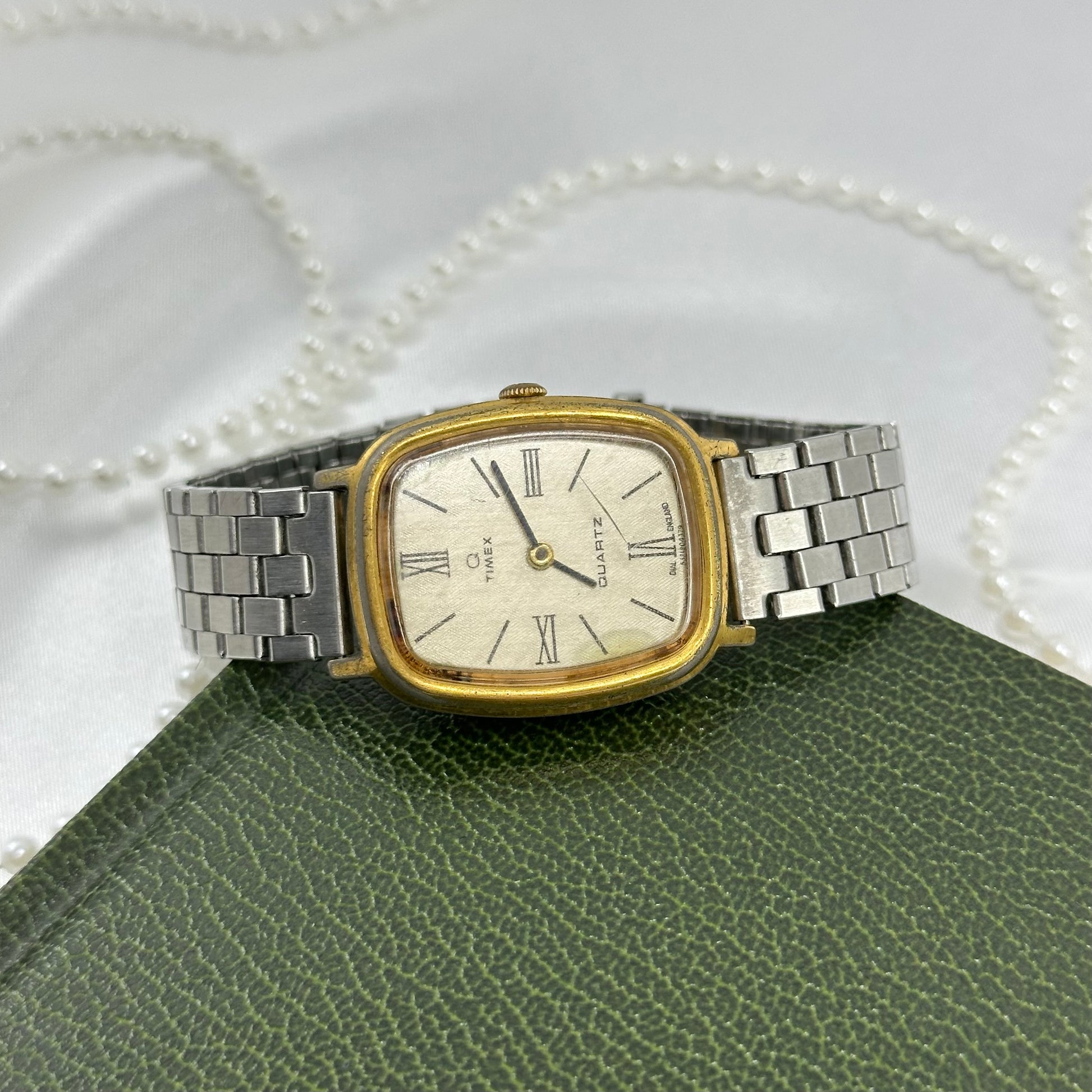 Vintage silver and gold tone Timex watch with rectangular dial, roman numeral markers, and unique metal clasp stretchable band.