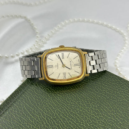Vintage silver and gold tone Timex watch with rectangular dial, roman numeral markers, and unique metal clasp stretchable band.
