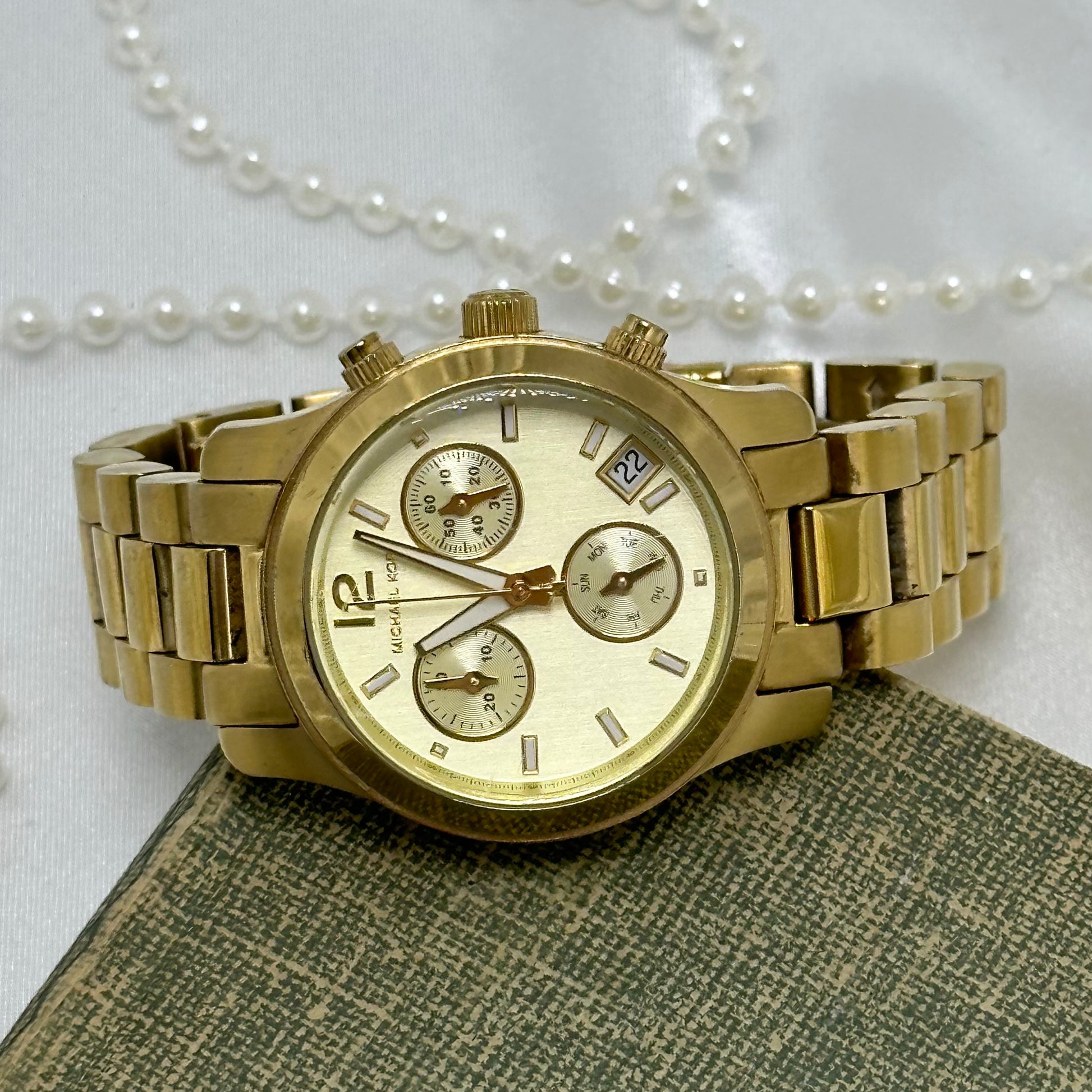 Vintage gold tone Michael Kors Runway stainless steel watch model MK5384 with double locking fold over clasp and date display. Case size is 33 mm. Buttons on the side start/stop the stopwatch dial at the bottom and reset the stopwatch hand. 5 ATM (50 meter) water resistant.