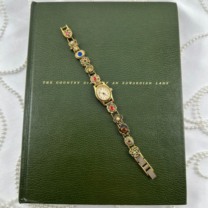 Rare vintage gold tone Avon watch with oval dial and multicolor slide charm band.