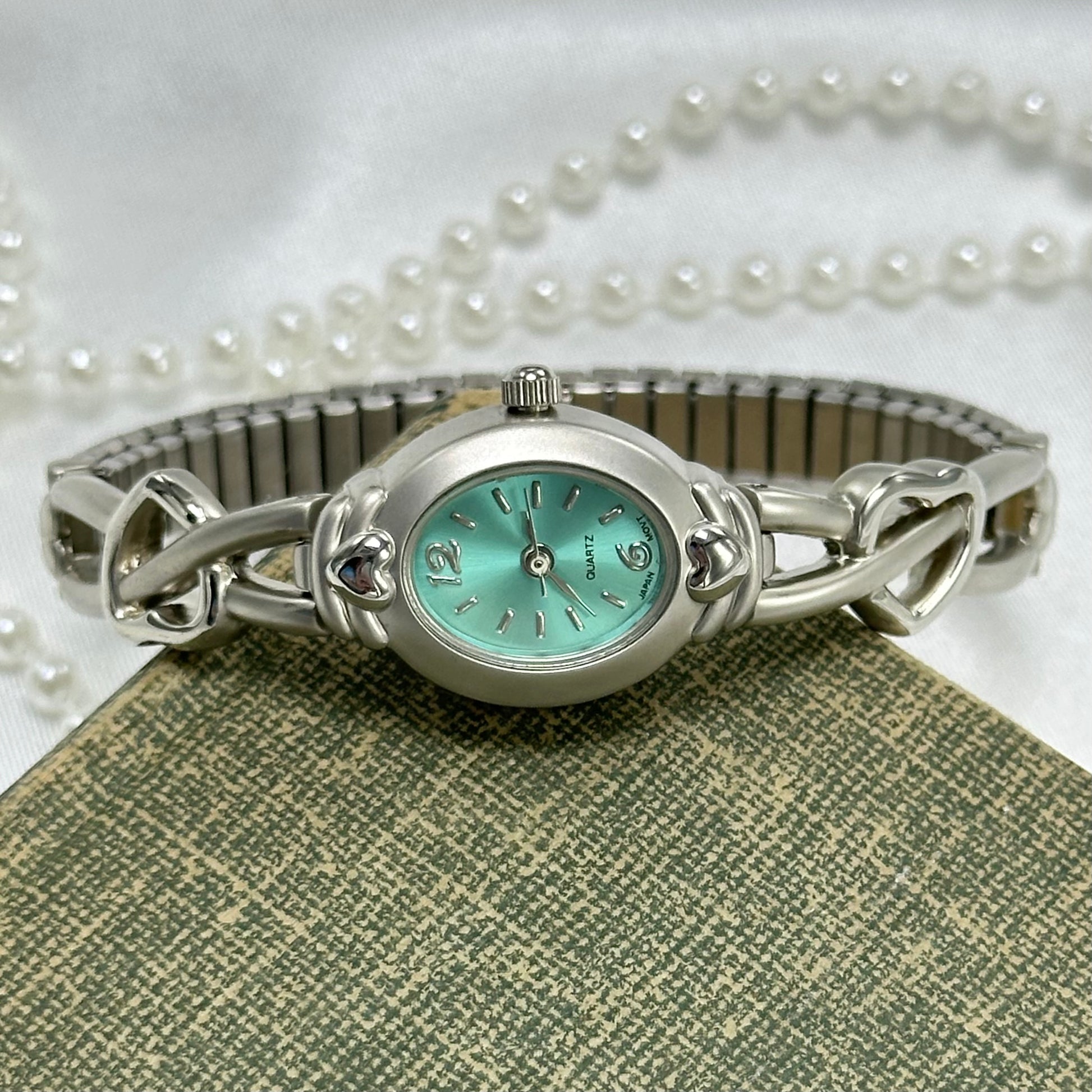 Dainty silver tone watch with heart band and quartz movement. Dial is a teal blue.