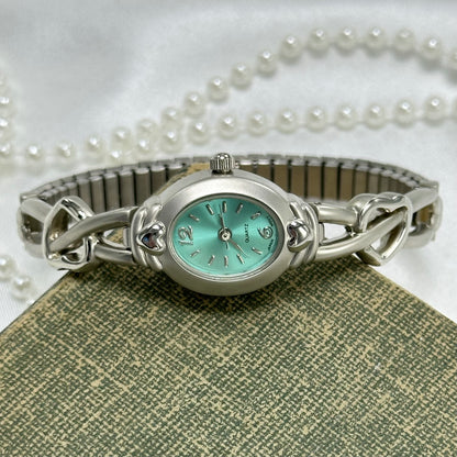 Dainty silver tone watch with heart band and quartz movement. Dial is a teal blue.
