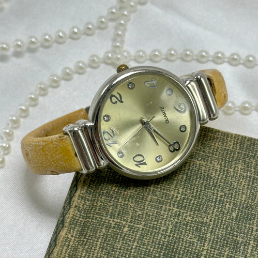 Silver tone round dial cuff watch with tan leather patterned band and quartz movement.