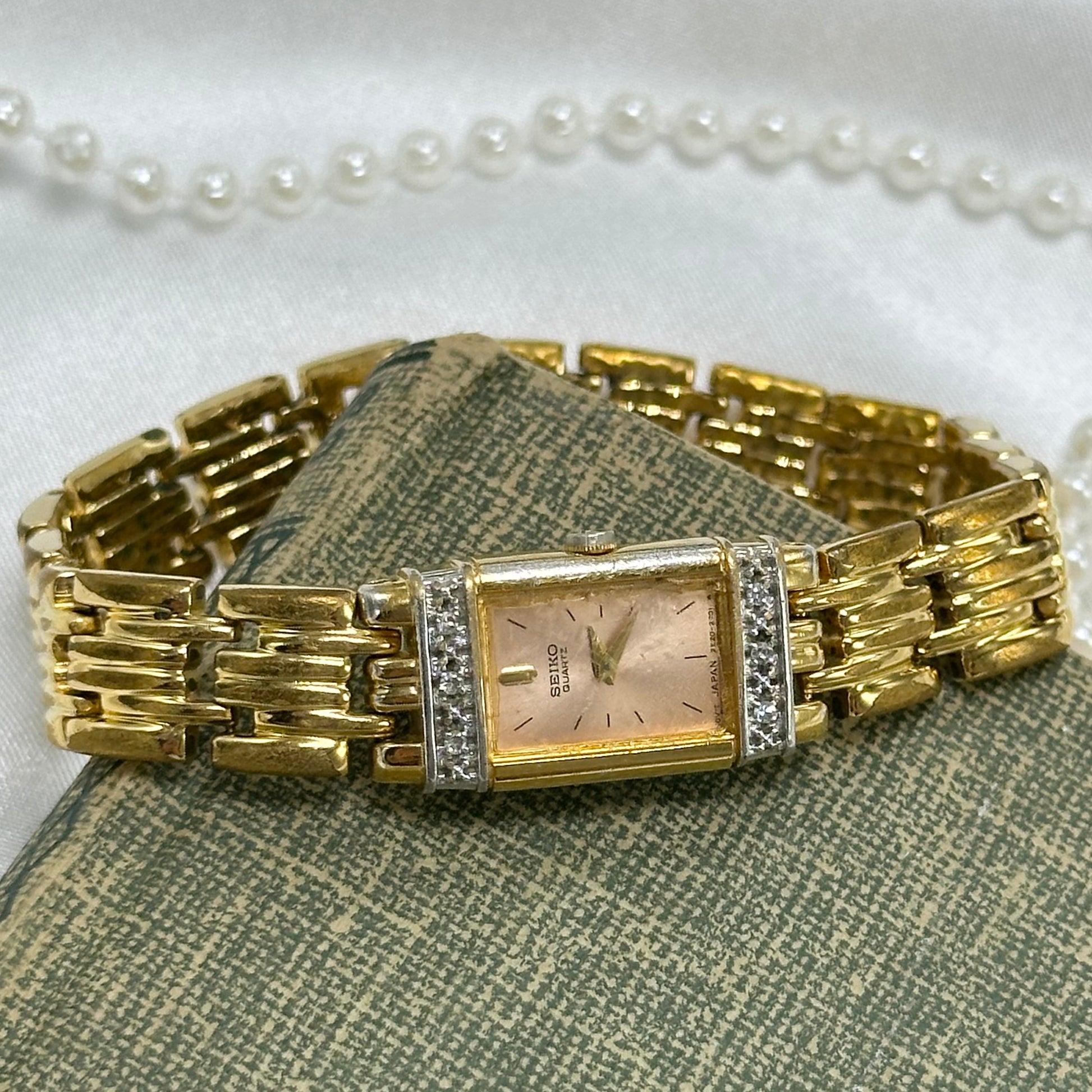 Gold tone diamanté Seiko watch with pink rectangle dial and clasp band.