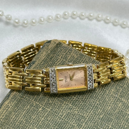 Gold tone diamanté Seiko watch with pink rectangle dial and clasp band.