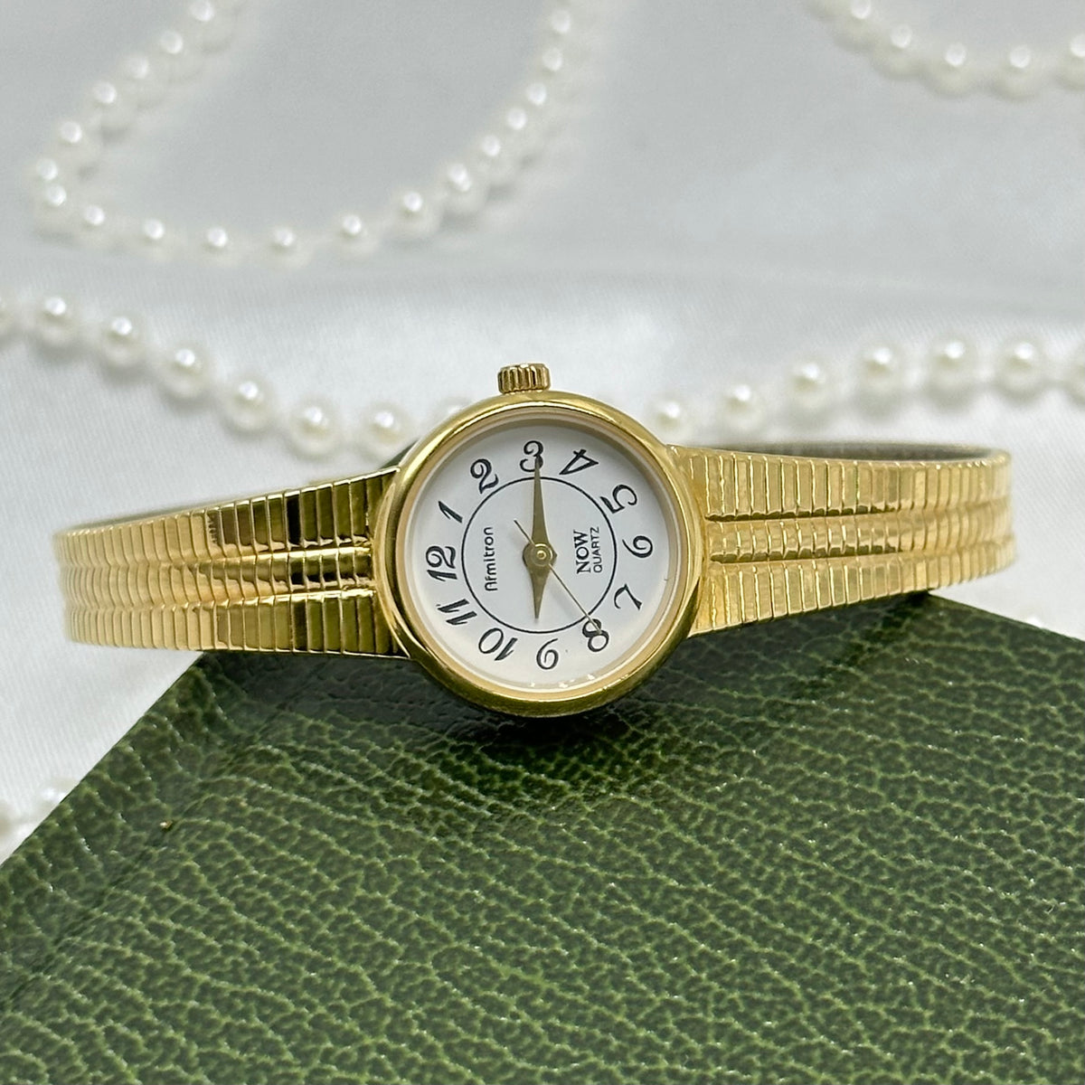 Vintage slender gold tone Armitron watch with round dial and metal clasp band.