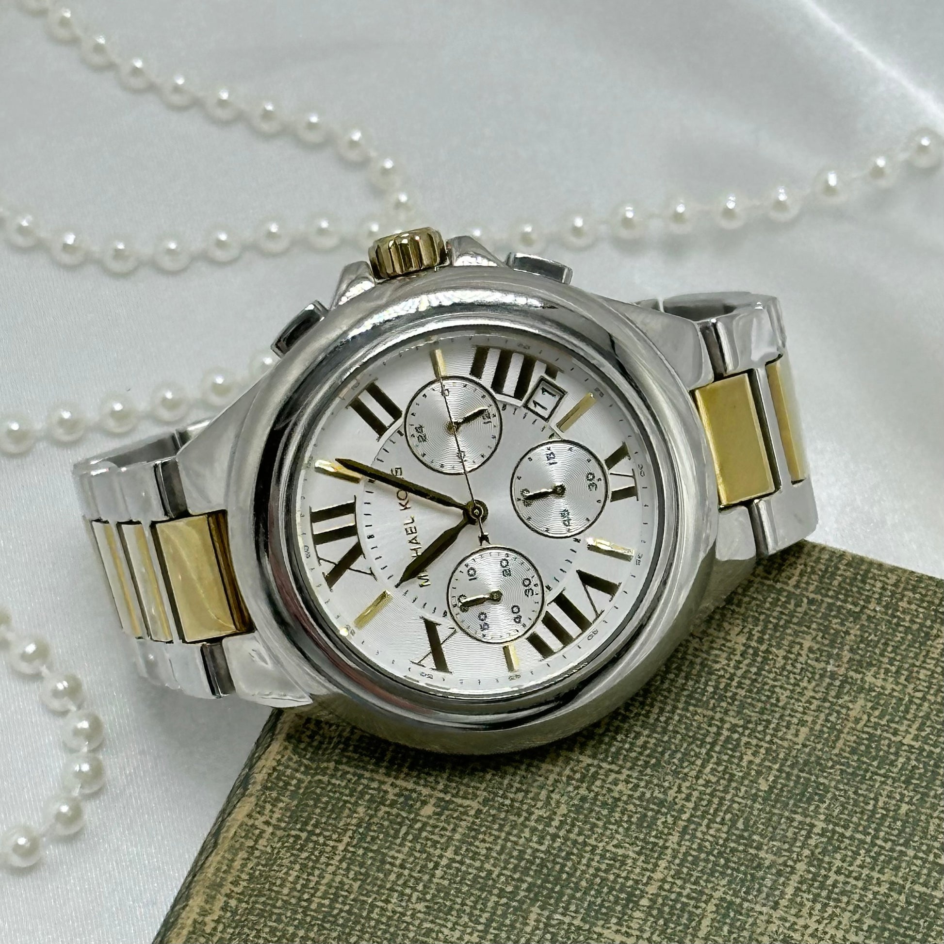 Vintage silver and gold tone Michael Kors MK-5653 tank stainless steel watch with roman numeral markers on round dial and double locking fold over clasp band. Date display. Buttons on the side start/stop the stopwatch dial at the bottom and reset the stopwatch hand.&nbsp;5 ATM (50 meter) water resistant.
