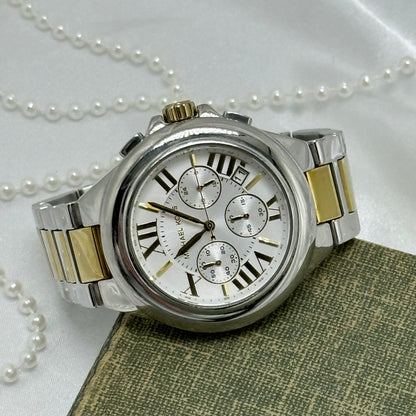 Vintage silver and gold tone Michael Kors MK-5653 tank stainless steel watch with roman numeral markers on round dial and double locking fold over clasp band. Date display. Buttons on the side start/stop the stopwatch dial at the bottom and reset the stopwatch hand.&nbsp;5 ATM (50 meter) water resistant.