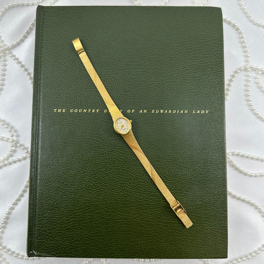 Gold tone vintage Elgin watch with swirl design band and oval dial.