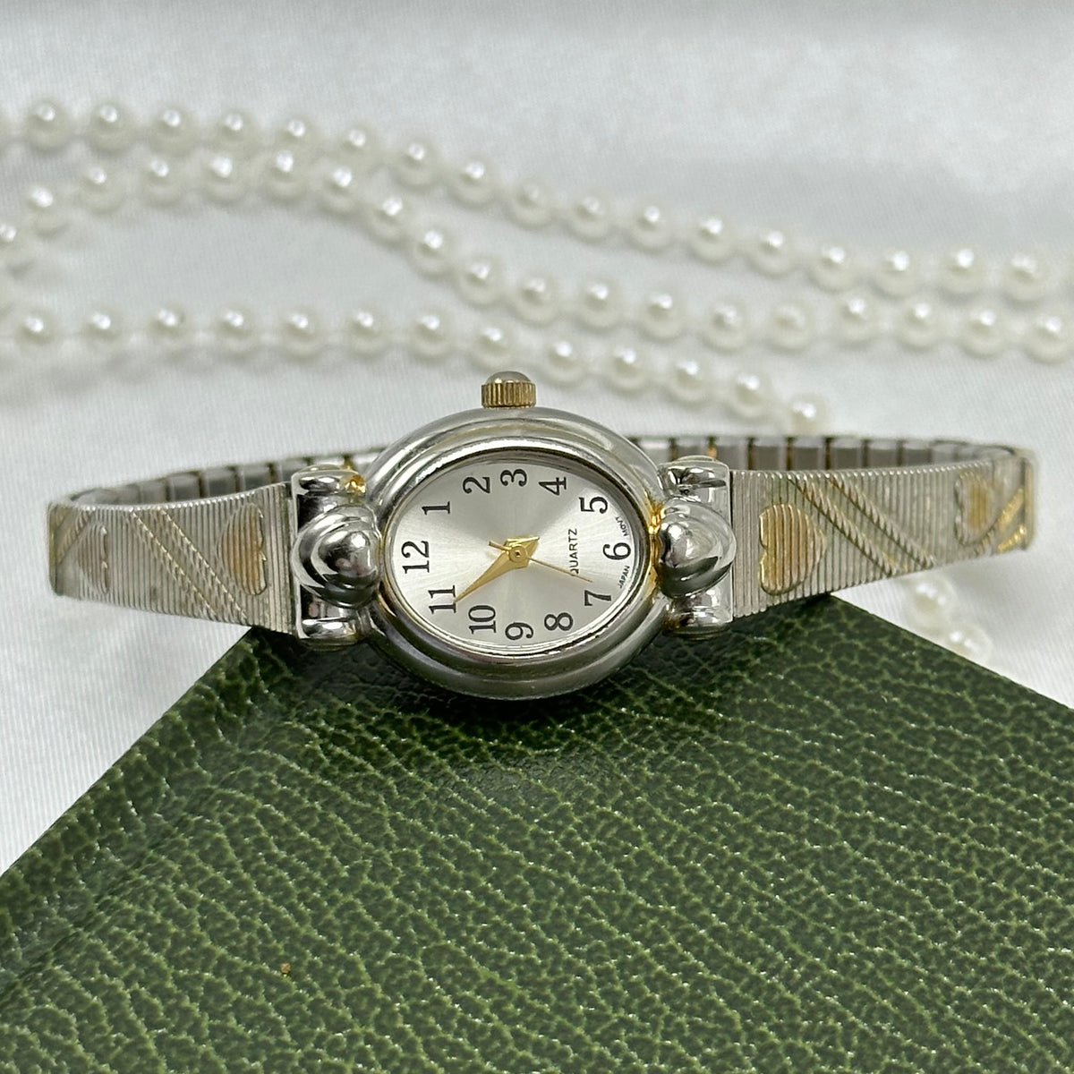 Dainty two-tone oval dial watch with silver and gold heart stretchable band and quartz movement.