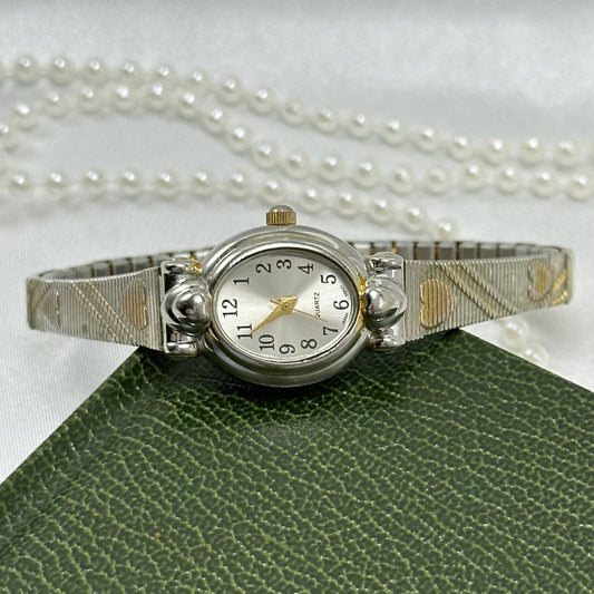 Dainty two-tone oval dial watch with silver and gold heart stretchable band and quartz movement.