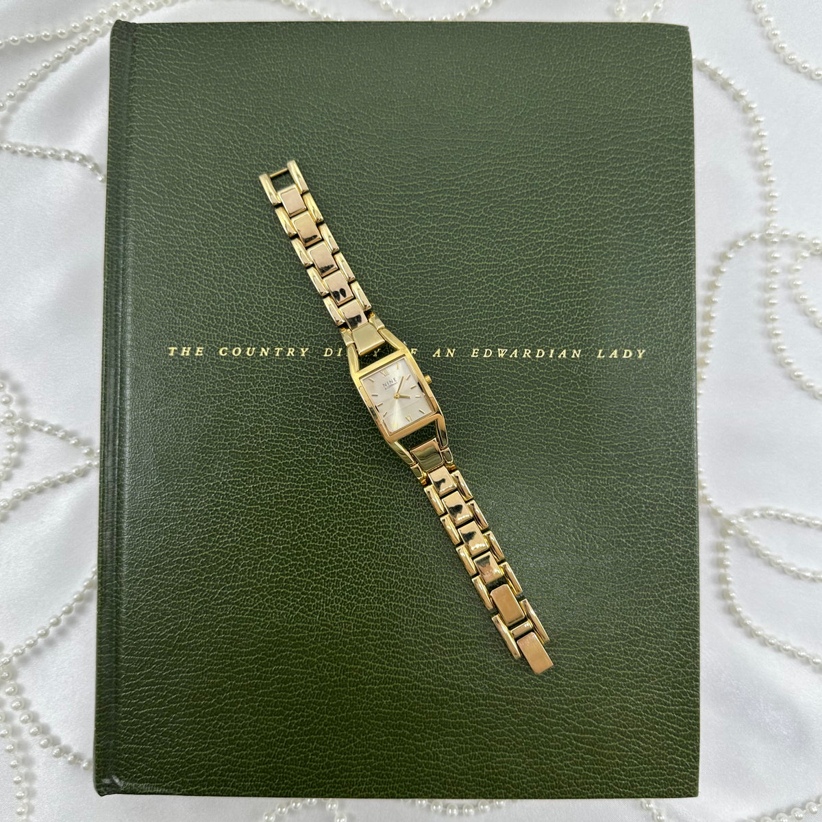 Gold tone Nine &amp; Company watch with rectangular dial and metal link band.