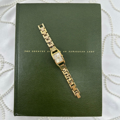Gold tone Nine &amp; Company watch with rectangular dial and metal link band.