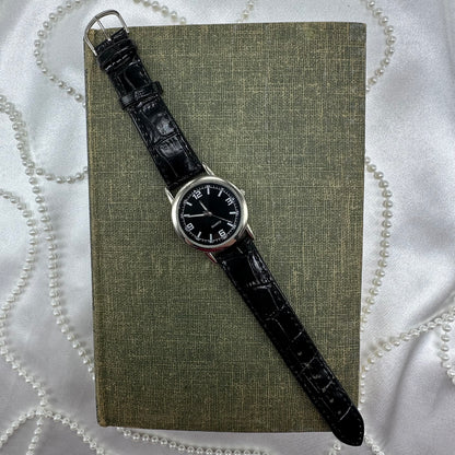 Silver tone watch with black dial and quartz movement.
