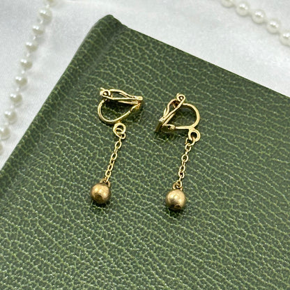 Dainty gold tone dangle clip on earrings with ball beads on chain.