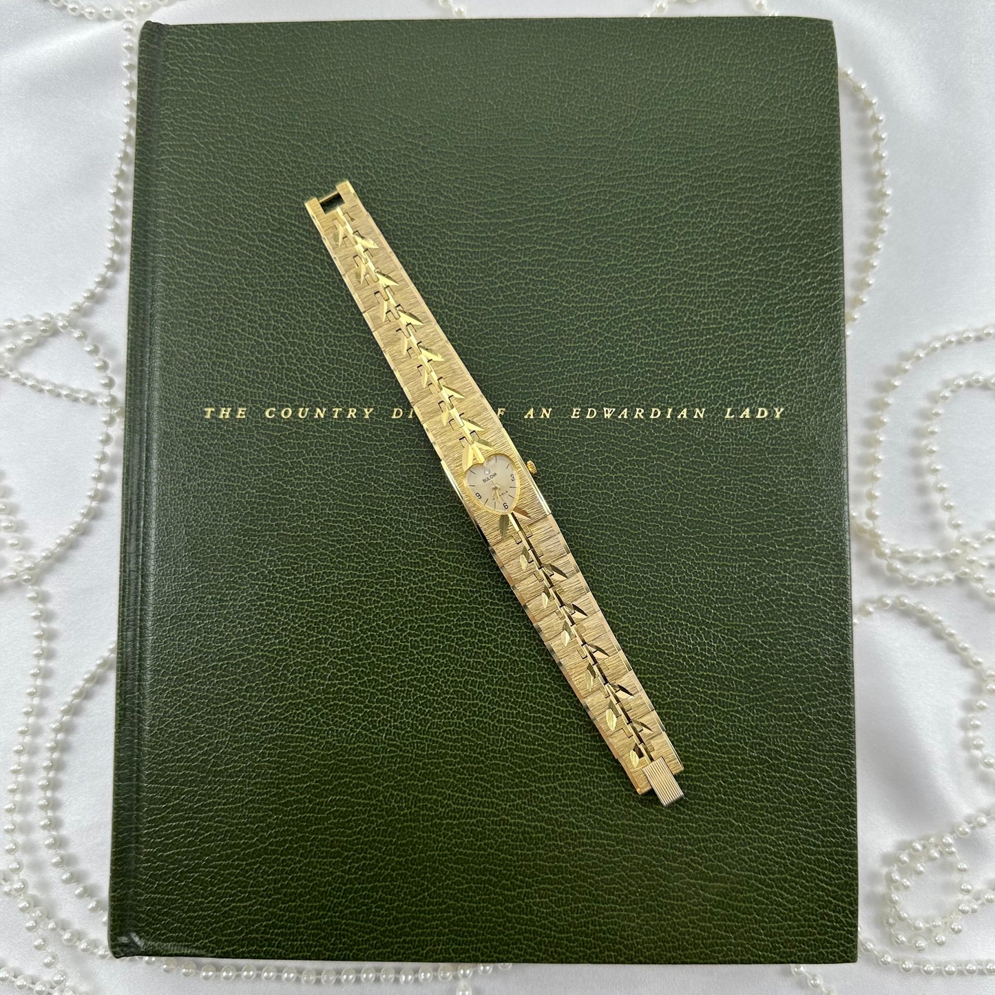 Vintage gold tone Bulova manual winding tank watch with vine pattern band and heart shaped dial.