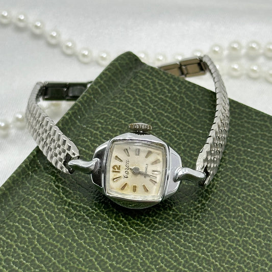 Vintage silver tone Caron manual winding watch with dainty square dial and metal clasp band.
