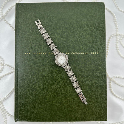 Vintage silver tone watch with round dial and angel charm band.