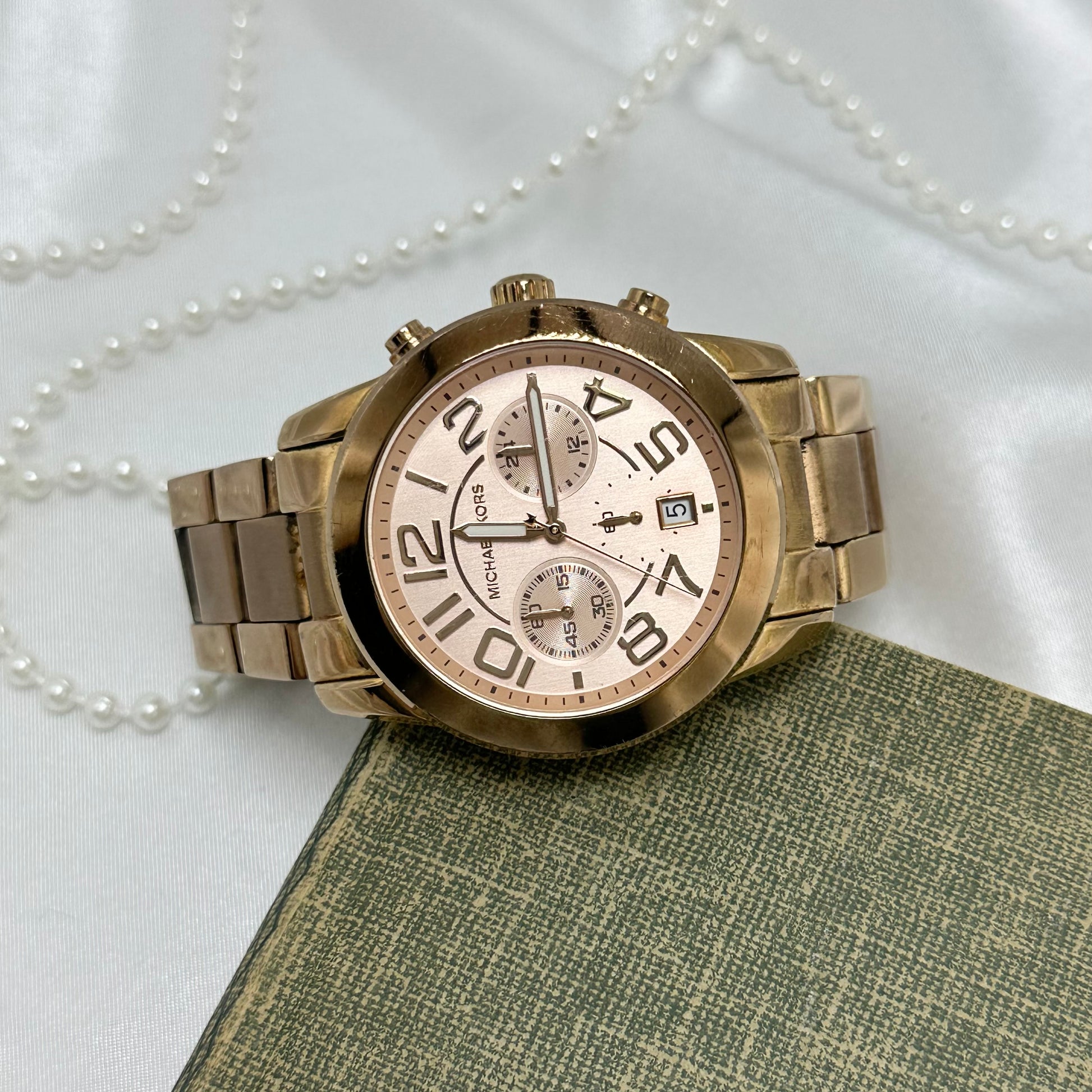 Vintage rose gold tone Michael Kors tank stainless steel watch model 5727 with round dial and double locking fold over clasp band. Date display. Buttons on the side start/stop the stopwatch dial at the bottom and reset the stopwatch hand. 10 ATM (100 meter) water resistant.