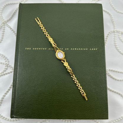 Gold tone Armitron watch with chevron style link band and oval mother of pearl dial.
