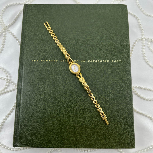 Gold tone Armitron watch with chevron style link band and oval mother of pearl dial.