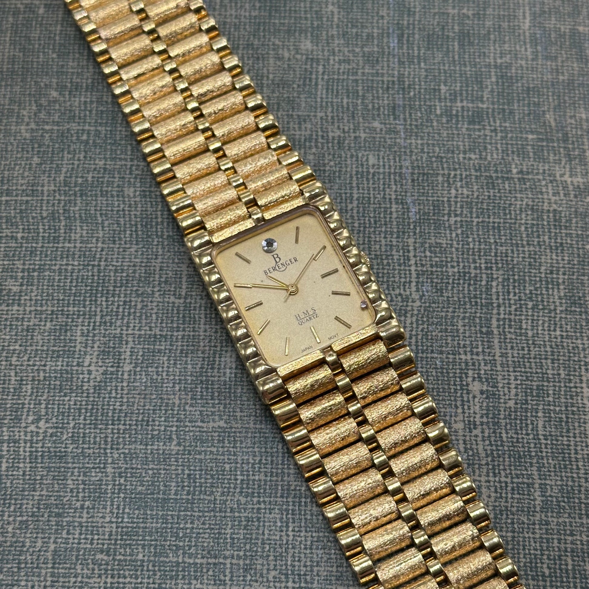Vintage gold tone chunky tank Berenger watch with rectangle dial and textured clasp band.