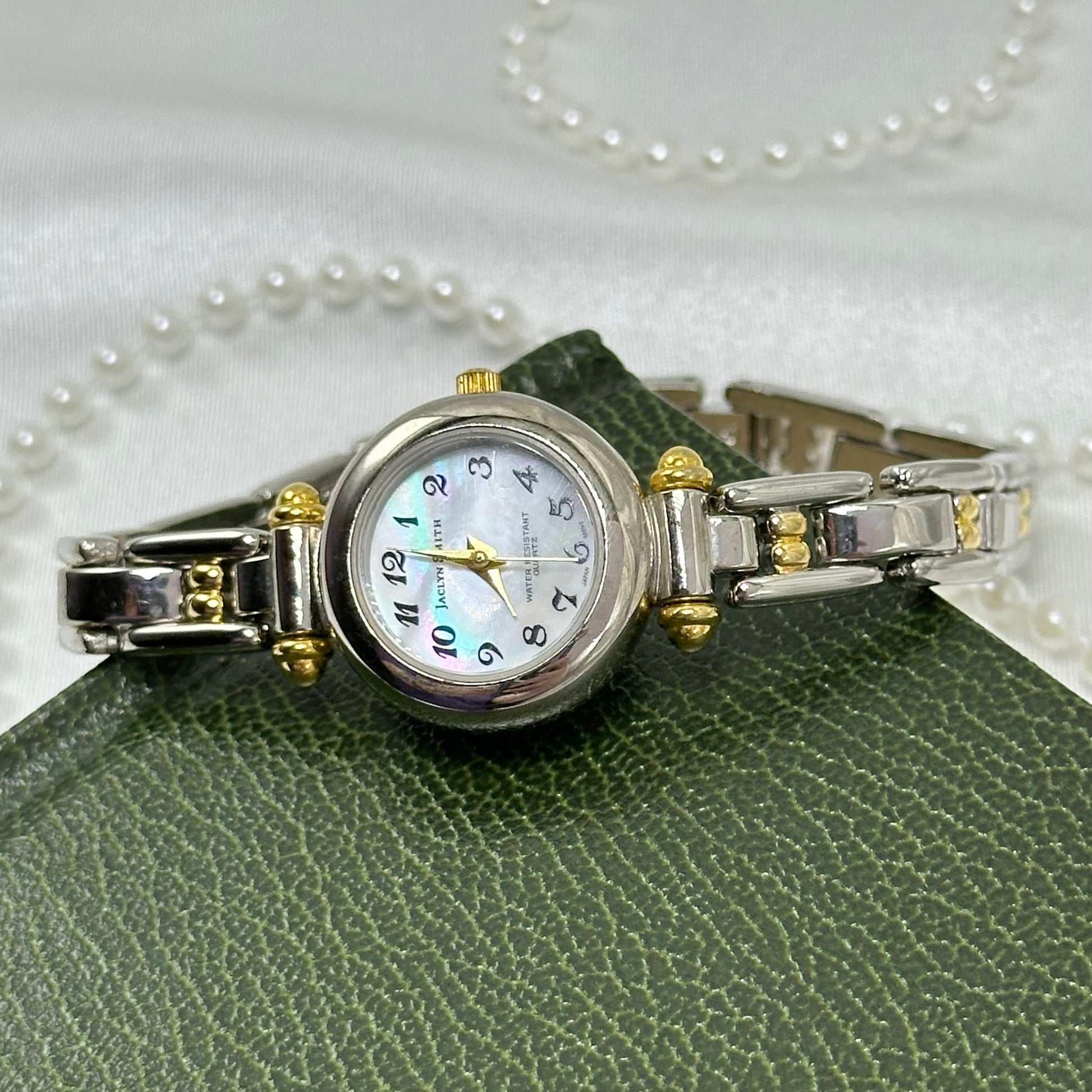 Silver and gold tone Jaclyn Smith watch with round mother of pearl dial and two-tone clasp band.