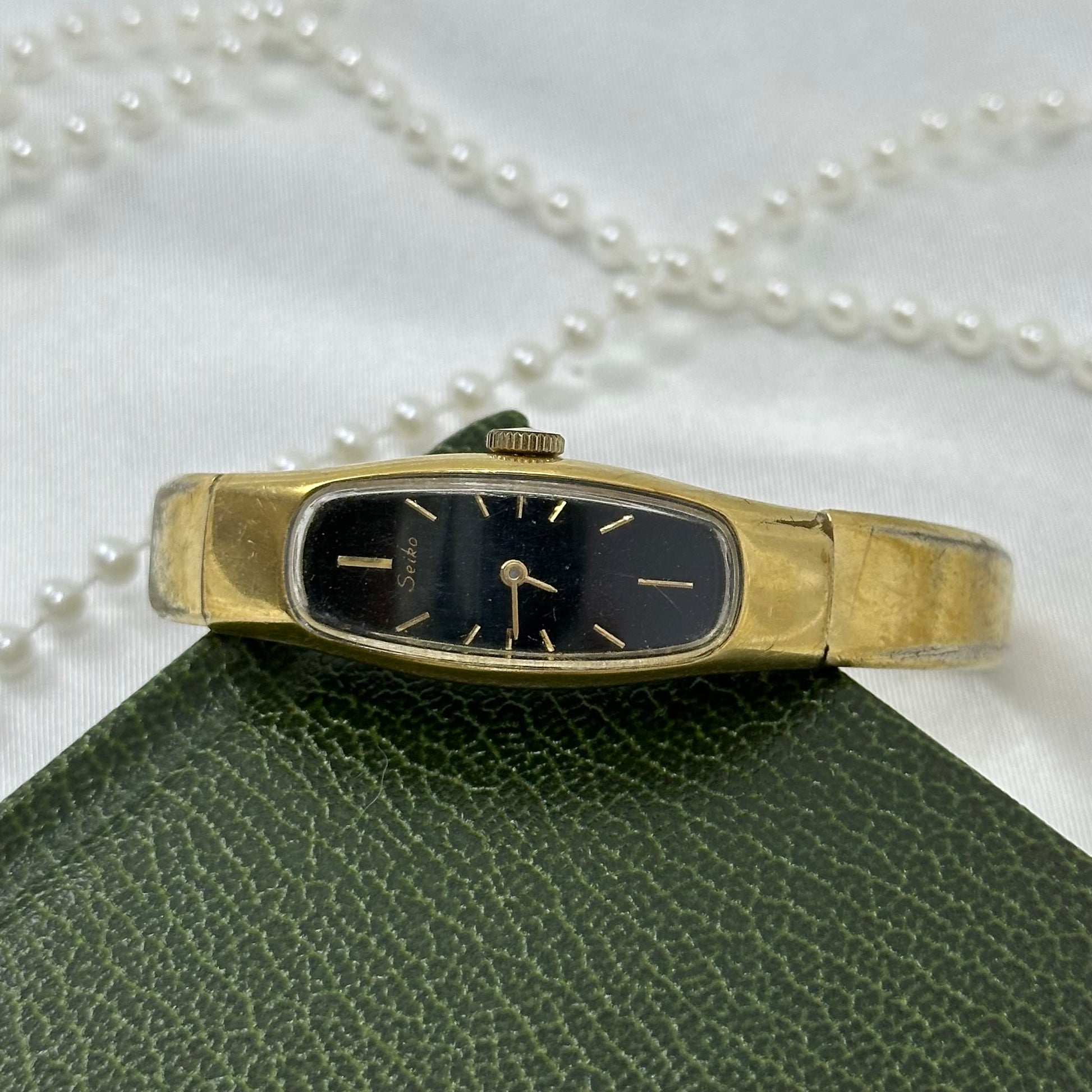 Vintage gold tone Seiko manual winding watch with bangle style band and black oval dial from the 1980's.