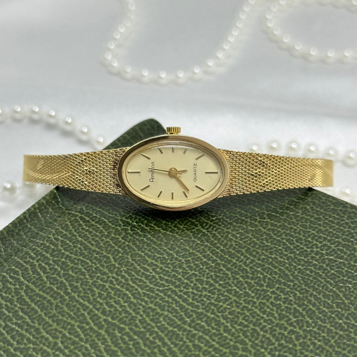 Vintage gold tone Armitron watch with slender oval dial and detailed floral mesh band.