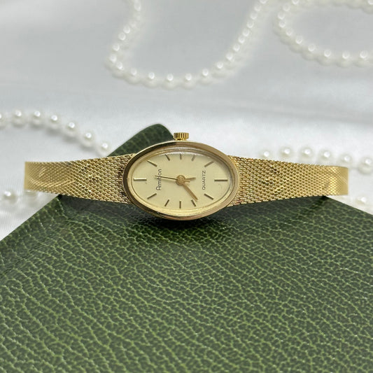 Vintage gold tone Armitron watch with slender oval dial and detailed floral mesh band.