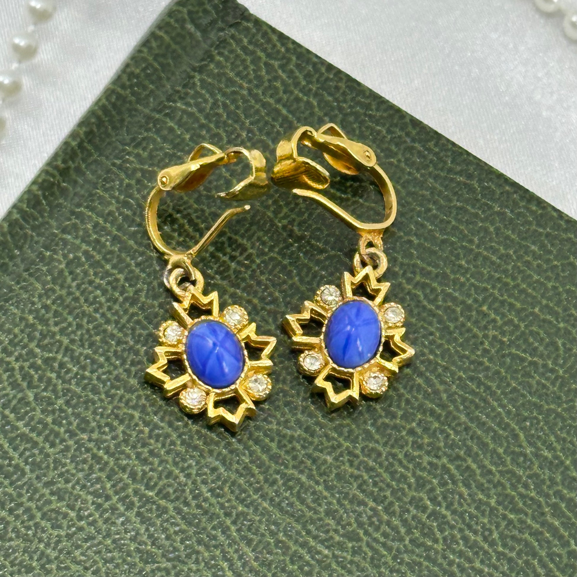 Vintage dangle gold tone clip on starburst earrings with clear and blue stones.