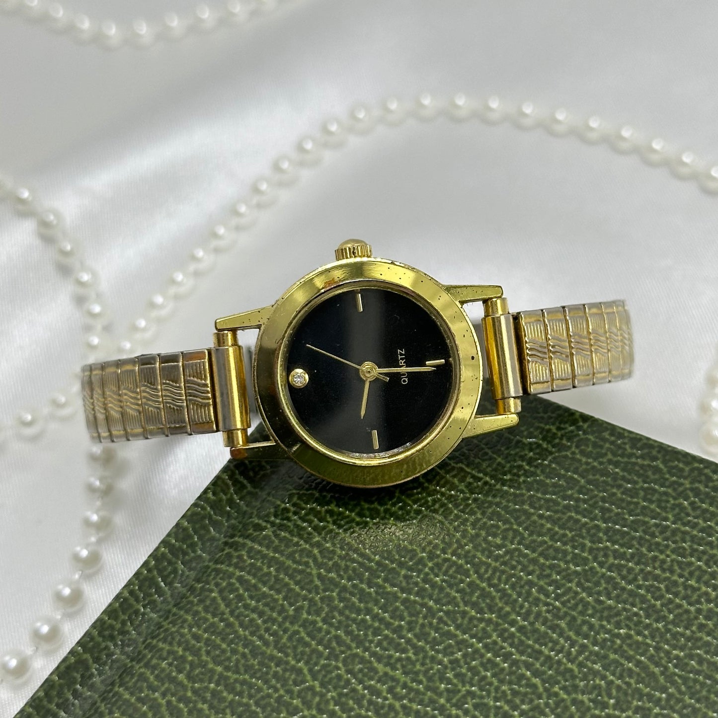 Classic gold tone watch with round black dial and stretchable band.