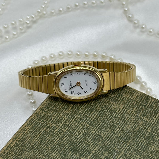 Dainty classic oval dial gold tone Timex watch with quartz movement and stretchable band.